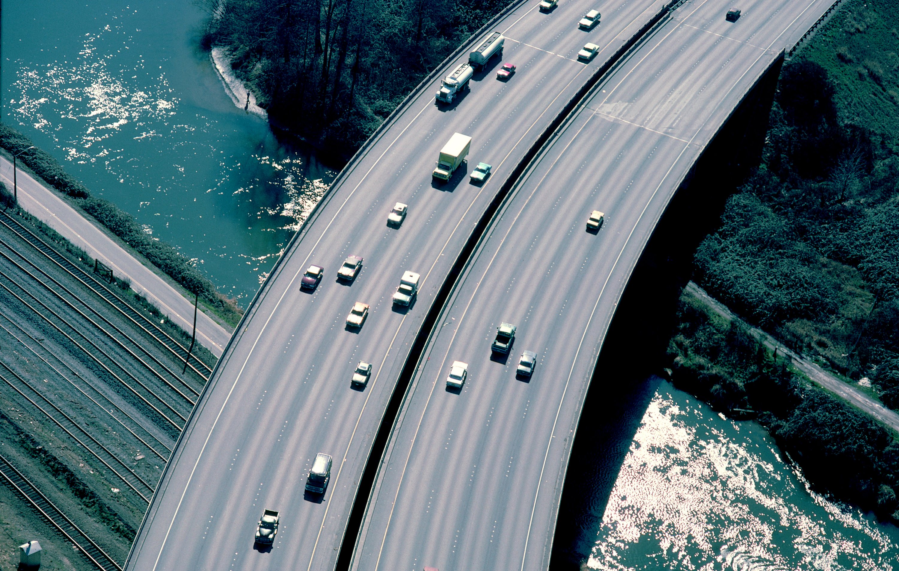 An aerial view of vehicles on a freeway bridge passing over a river.